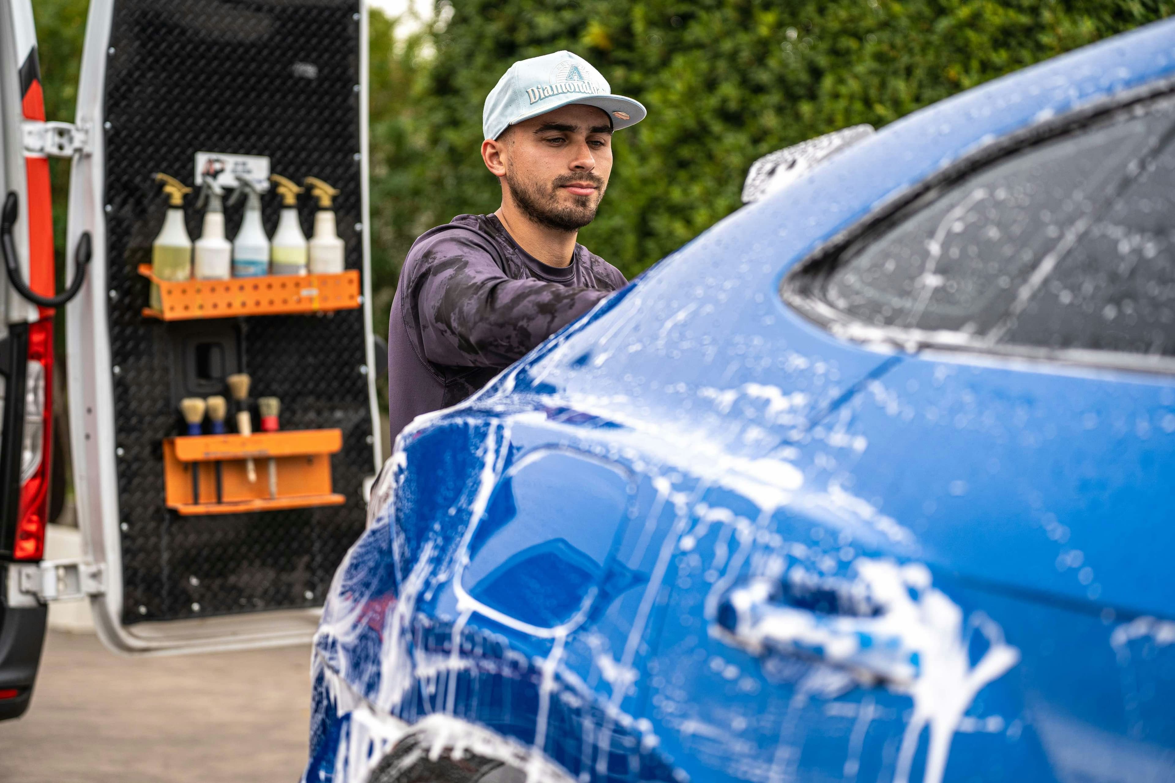 A car detailer washing a blue car beside cleaning supplies